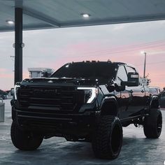 a large black truck parked in a parking lot next to a gas station at dusk