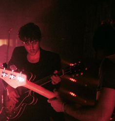 two people playing guitars in a dark room