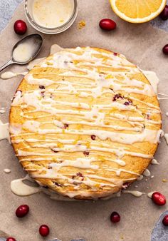 a cake with icing and cranberries sitting on top of a piece of parchment paper