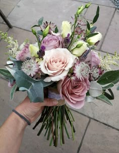 a person holding a bouquet of flowers in their hand on the ground with other flowers and greenery