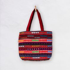 The Akha-Ani large tote bag is the perfect everyday cotton carry-all. It's generous size is designed to hold all the essentials or a lot...! The decoration on the exterior of the bag is hand crafted by the Akha people who live in the hills of  Myanmar. The pattern is colourful and embroidered with different coloured fabrics and threads. *  Bag 46cm Wide x 40cm Depth *  27cm handles *  Inside Bag large open pocket 21cm X 21cm *  Inside zippered pocket 21cm X 21cm *  Also Drawstring compartment in middle of bag *  Cotton with woollen and cotton embroidery *  Padded Base *  Select from a range of woven colour variations Care: Dry Clean only Made in Burma | Fair Trade Disclaimer: Mingalaba products are all made by individual artisans. Each Bag is unique and it's very rare we see 2 perfectly id Red Embroidered Bag For Daily Use, Red Handwoven Shoulder Bag For Everyday Use, Red Handwoven Shoulder Bag, Red Embroidered Bags For Shopping, Embroidered Cotton Shopping Bags, Red Embroidered Shopping Bags, Large Capacity Red Tote Beach Bag, Embroidered Red Tote Bag, Red Handwoven Tote Bag