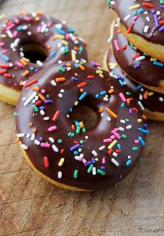 three donuts with chocolate frosting and sprinkles on a wooden surface