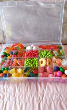 a plastic container filled with lots of different types of candies and candy beans on a bed