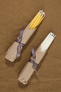 two yellow and white candles wrapped in brown paper with ribbon on the ends, sitting next to each other