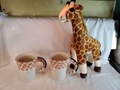 a stuffed giraffe next to two coffee mugs on a white tablecloth