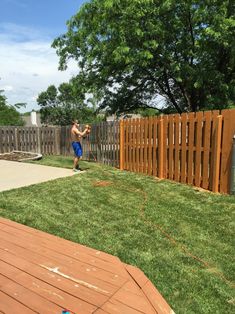 a man standing on top of a lush green field next to a wooden fence and grass covered yard