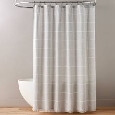 a white shower curtain in a bathroom with wood flooring and gray wall behind it