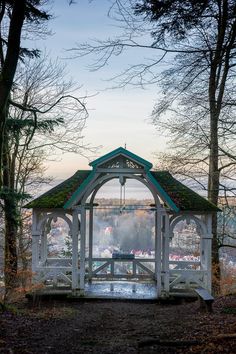 a gazebo in the middle of a wooded area with trees and water behind it