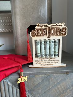 a graduation card holder with money in front of it and a red tassel hanging from the top