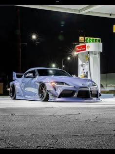 a blue sports car is parked in front of a gas station at night with its lights on