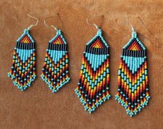 three pairs of beaded earrings on top of a brown surface with one earring in the shape of a feather