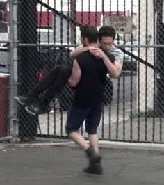 two men hugging each other in front of a fence