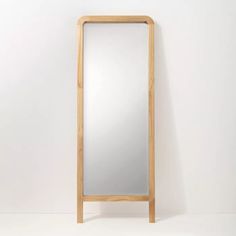 a tall wooden mirror sitting on top of a white floor next to a wall mounted shelf