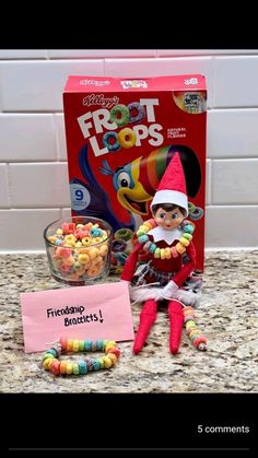 an elf is sitting on the counter next to some cereal and a sign that says, froot loops