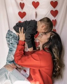 a woman holding a baby in her arms and kissing it's face with hearts on the background