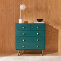 a green chest of drawers sitting on top of a wooden floor next to a lamp