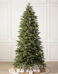 a christmas tree with presents under it on a wooden floor in front of a white wall