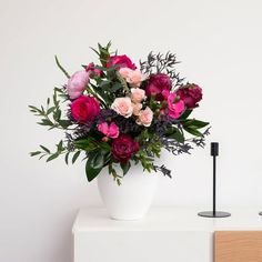 a white vase filled with lots of pink and red flowers on top of a table