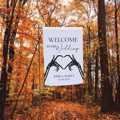 a welcome to our wedding sign hanging from a metal pole in the middle of an autumn forest