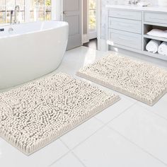 two bathroom rugs on the floor in front of a bathtub and sink area