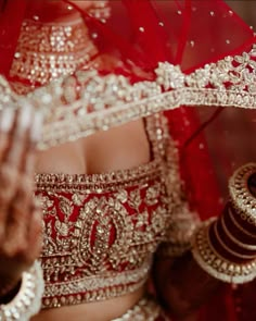 a woman in a red and gold bridal outfit holding her hands out to the side