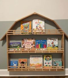 a wooden shelf with books on it in the shape of a house, against a gray wall