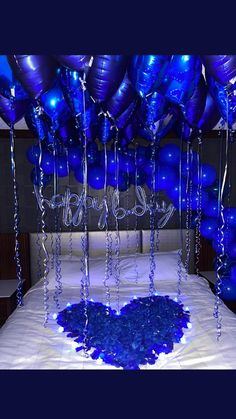 blue balloons and streamers are hanging from the ceiling above a bed with white sheets