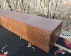 a wooden bench sitting on top of a rug in front of a forest filled with trees