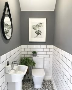 the bathroom is decorated in white and gray tile with black accents, including a mirror above the two toilets