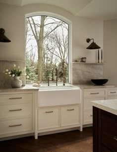 a kitchen with white cabinets and an open window looking out onto the trees outside,