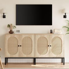 a tv mounted on the wall above a wooden cabinet with two speakers and a plant