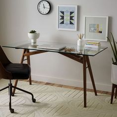 a desk with a glass top and wooden legs in front of a clock on the wall