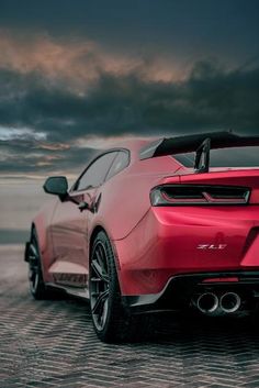 the rear end of a red sports car parked on a cobblestone road at dusk