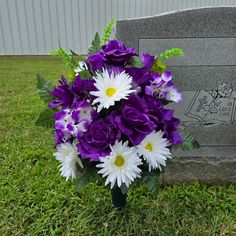 a bouquet of purple and white flowers sits in front of a headstone on the grass