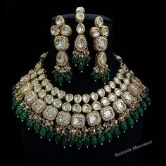 a necklace and earring set with green stones, pearls and emeralds on a black background