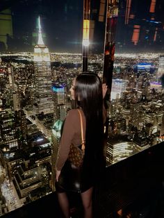 a woman standing on top of a tall building looking at the city lights and skyscrapers