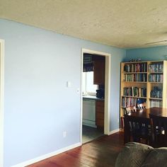 a living room filled with furniture and bookshelves next to a doorway that leads to a kitchen