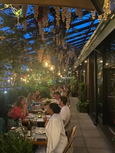 many people are sitting at tables in a restaurant with lights hanging from the ceiling above them