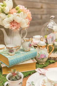 a table topped with books and vases filled with flowers next to teapots