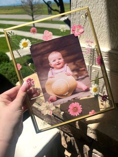 a person holding up a card with a baby in it and flowers on the front