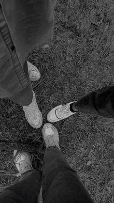 two people standing next to each other in the grass with their feet on one another