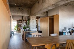 a wooden table and chairs in a room with concrete walls, wood flooring and open shelves