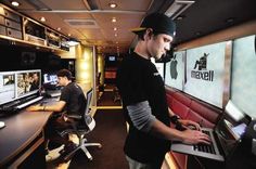 two men sitting in front of laptops on a desk with multiple monitors and television screens