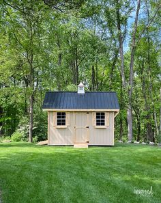 a small wooden shed sitting in the middle of a lush green field next to trees