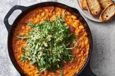 a skillet filled with pasta and garnished with parsley next to slices of bread