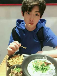 a young boy sitting at a table eating food with chopsticks in front of him