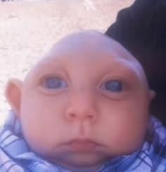 a close up of a baby with blue eyes and a scarf around his neck looking at the camera