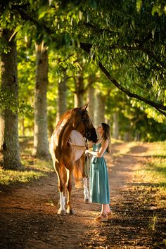 a woman is petting a horse on the side of a dirt road with trees in the background