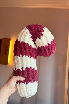 a hand holding up a red and white knitted object in front of a wall