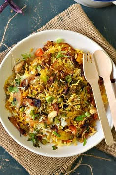 a white bowl filled with rice and vegetables next to a wooden utensil on top of a blue table cloth